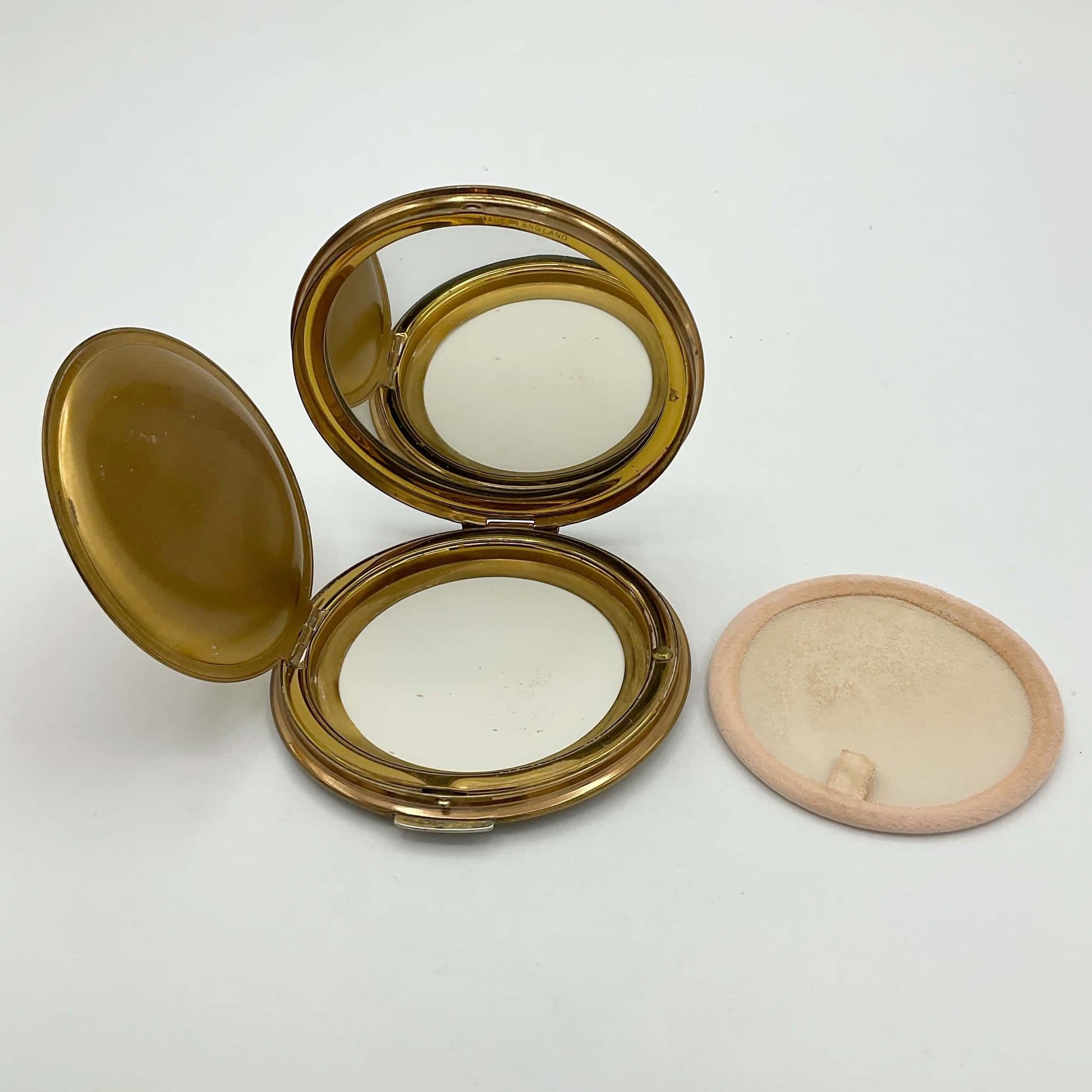 open powder compact showing a clear mirror, a clean powder area and a powder screen