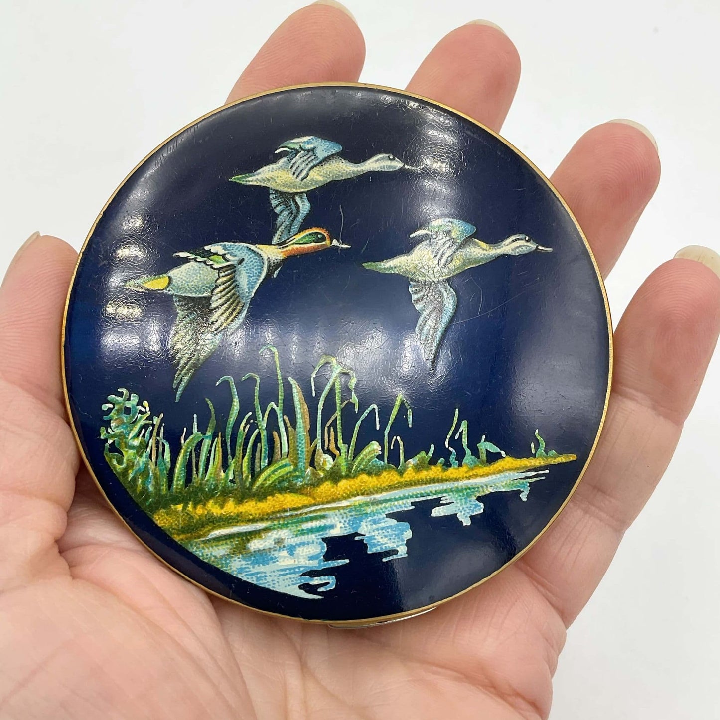 beautiful enamel featuring three ducks flying over water on a mirror compact lid held in a hand