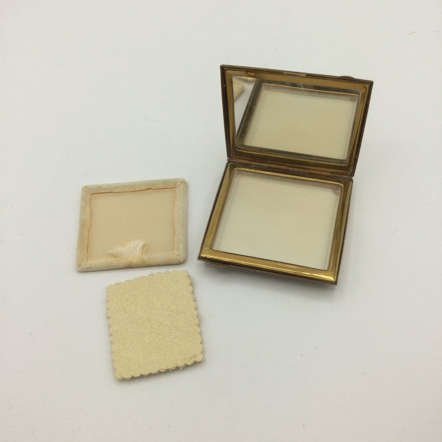 open Zenette powder compact showing a mirror, unsed powder screen and applicator
