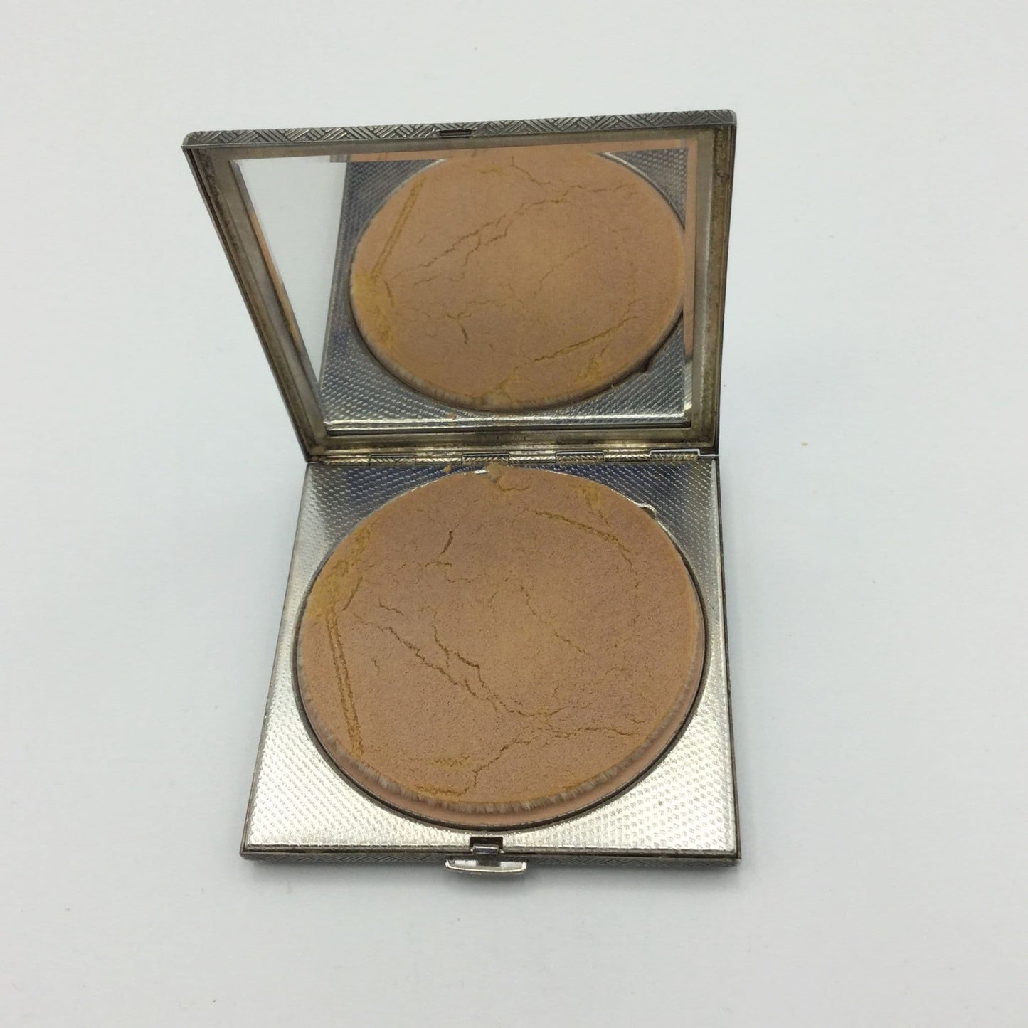 A silver coloured square compact with the lid open showing the mirror and applicator sponge