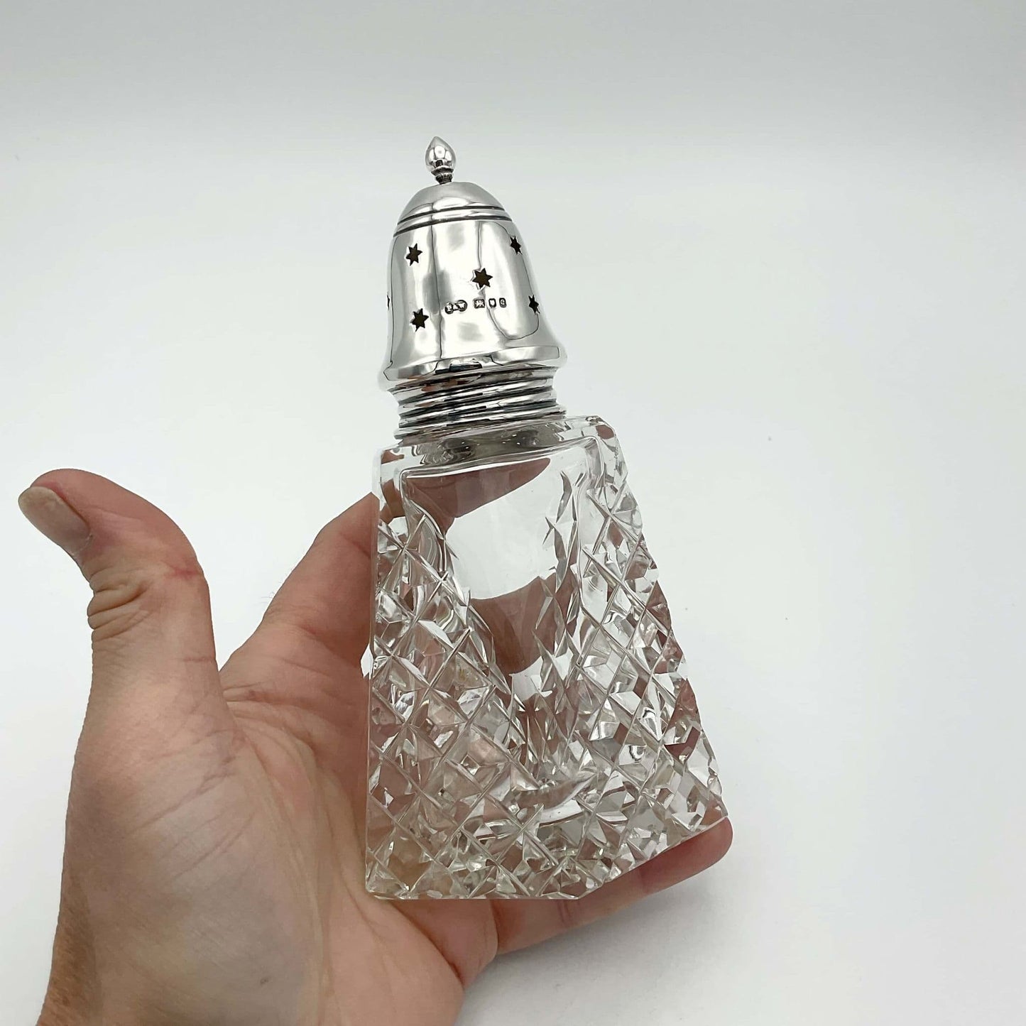 Vintage silver topped glass sugar shaker held in a hand