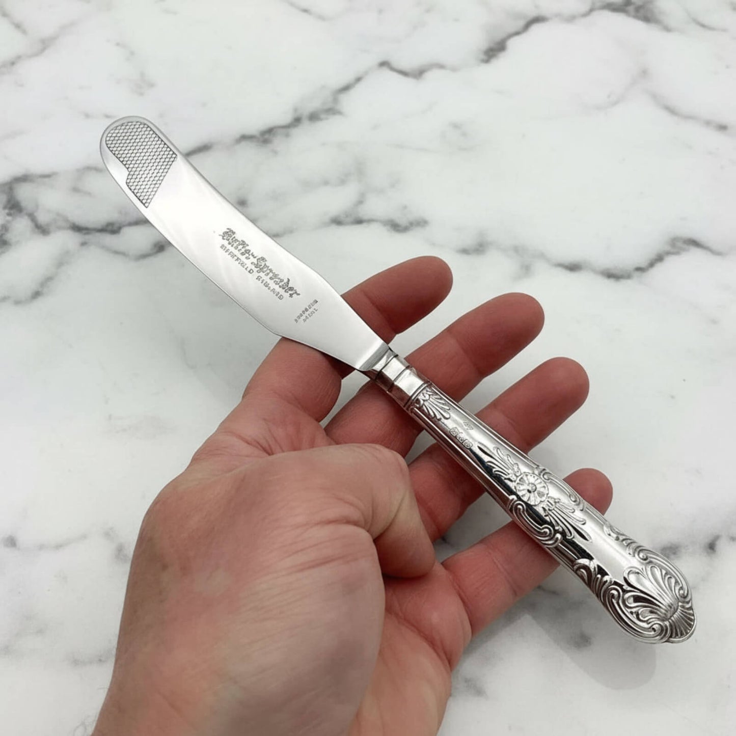 Vintage 1978 Sterling Silver Handled Butter Knife held in a hand on a marble background