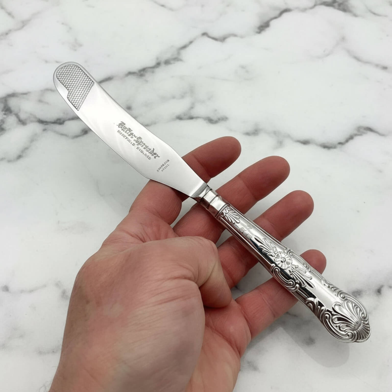 Vintage 1978 Sterling Silver Handled Butter Knife held in a hand on a marble background