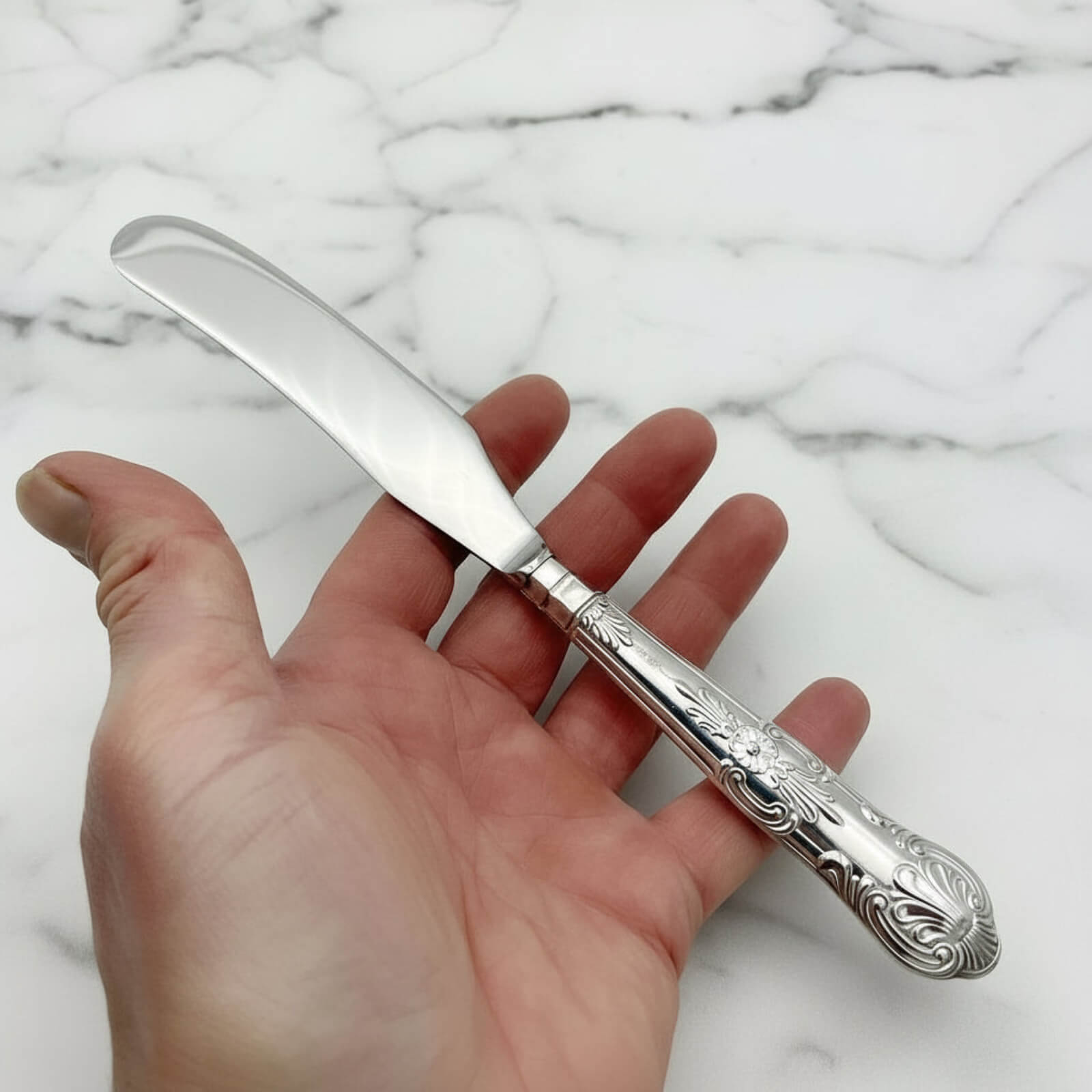 Vintage 1978 Sterling Silver Handled Butter Knife held in a hand on a marble surface