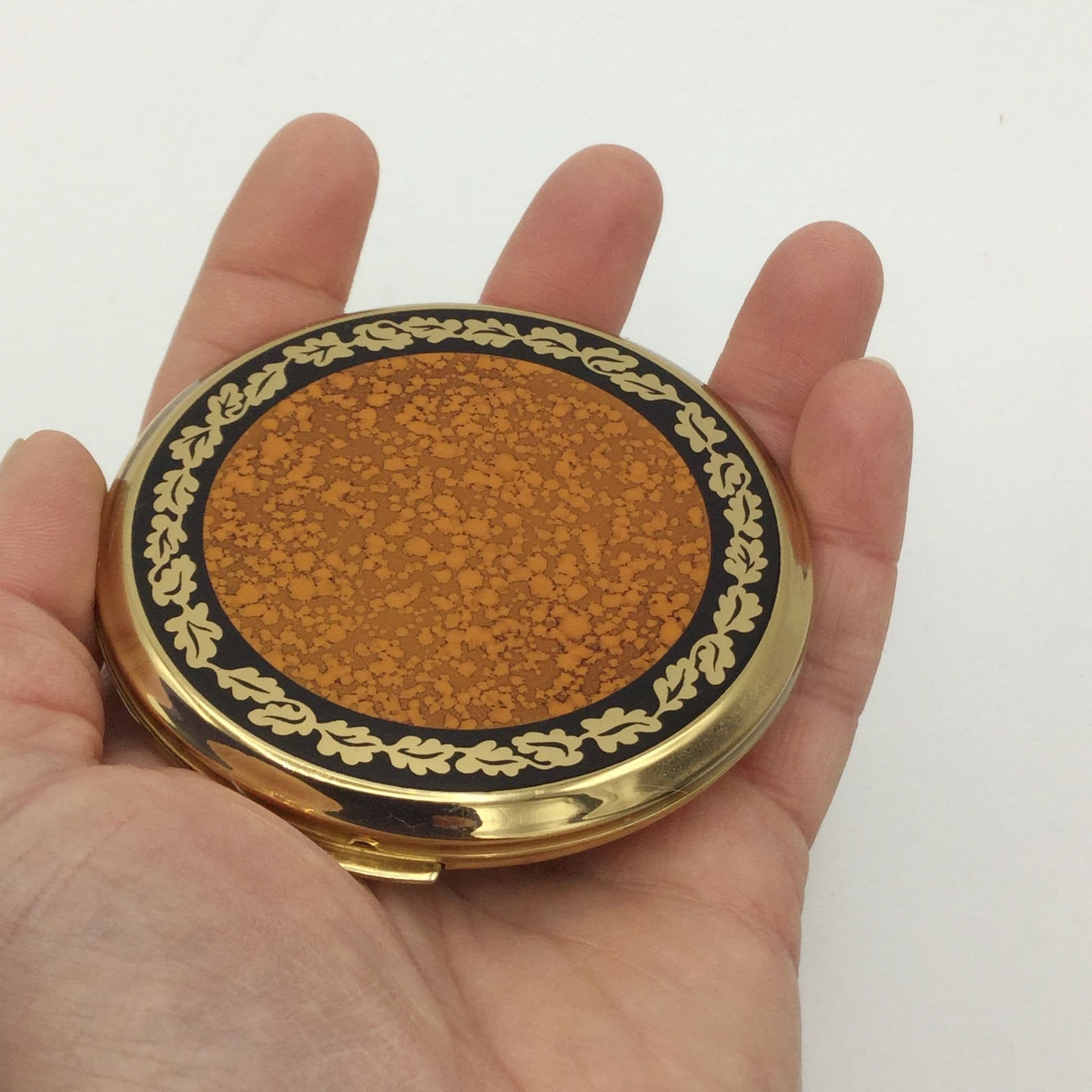 Bright 1990s vintage Stratton compact in a hand with an orange and brown enamel
