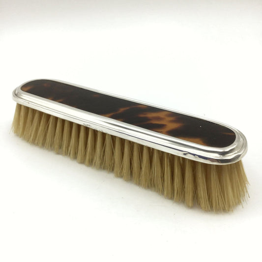 Antique clothes brush with a brown and back tortoiseshell back and a silver edge on a white background