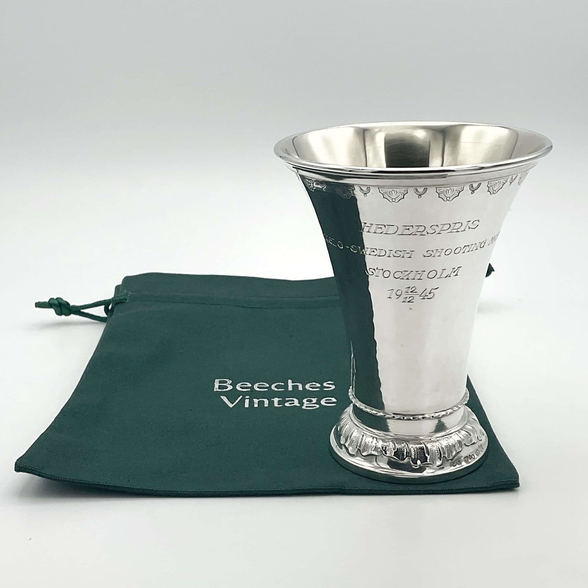 Silver fluted shape vase or cup standing on a green Beeches Vintage cotton bag. The vase has Hederspris Anglo - Swedish Shooting Match Stockholm 12/12 1945 engraved in the centre.