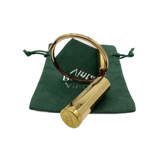A gold coloured lipstick case with a mirror attached to the end sitting on a green cotton bag. The mirror is showing a reflection of the bag and the end of the lipstick has Stratton No 2 on it.