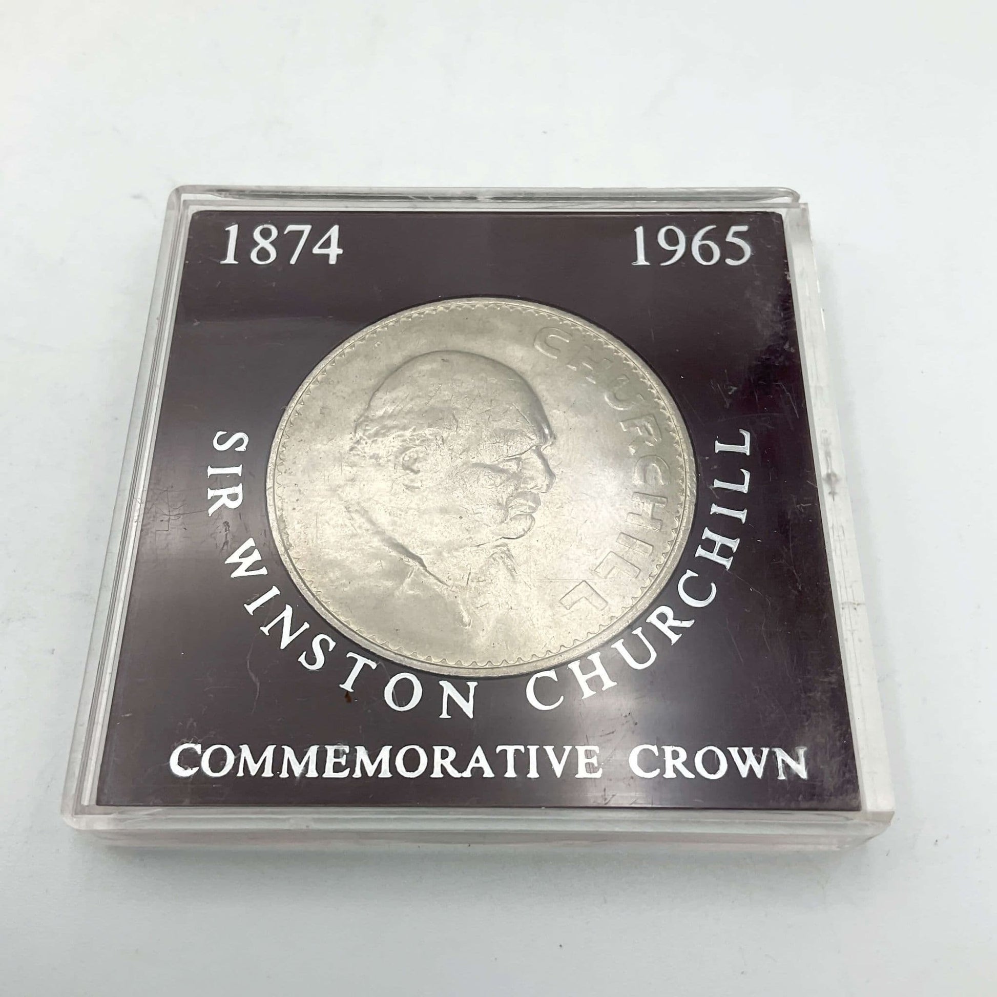 Silver coloured coin with Winston Churchill's head on it in a dark red case