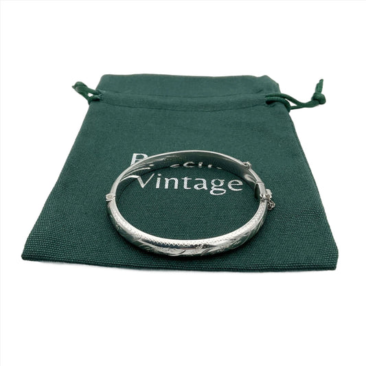 Silver bracelet with etched pattern on a green bag