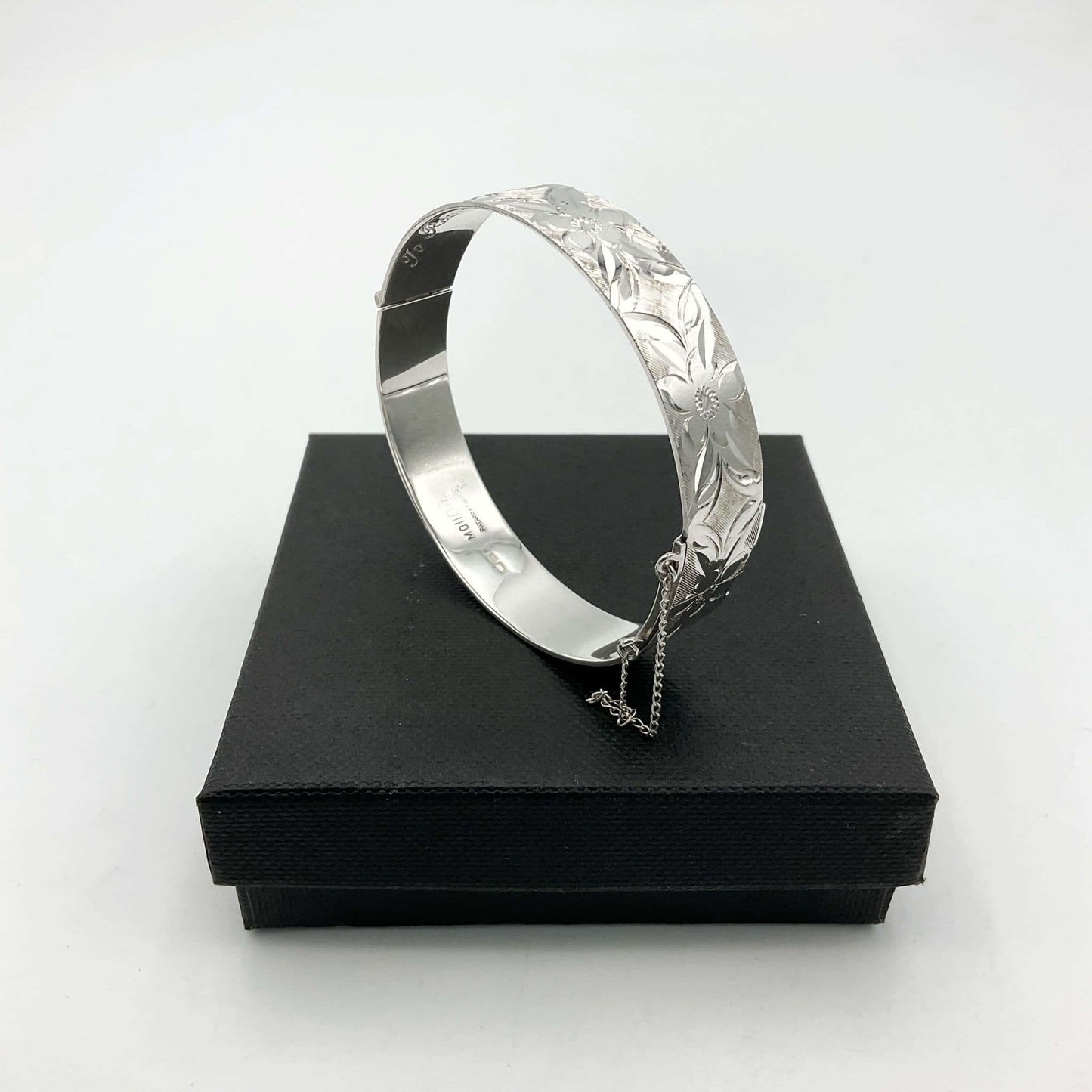 Silver bracelt with engraved flowers sitting on a black box