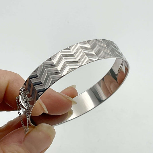 Silver bracelet with zig zag pattern being held by fingertips