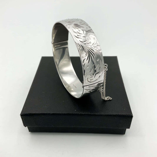 Wide Silver bracelet with brightcut pattern sitting on a black box