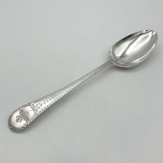 Large antique silver serving spoon with an engraved handle on a grey background