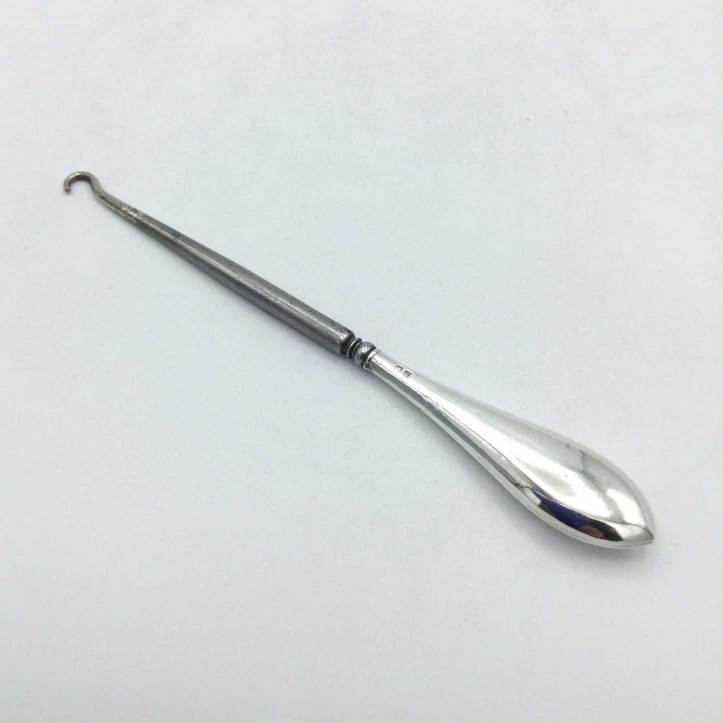 Silver handled button hook with a shiny handle and steel hook on a white background