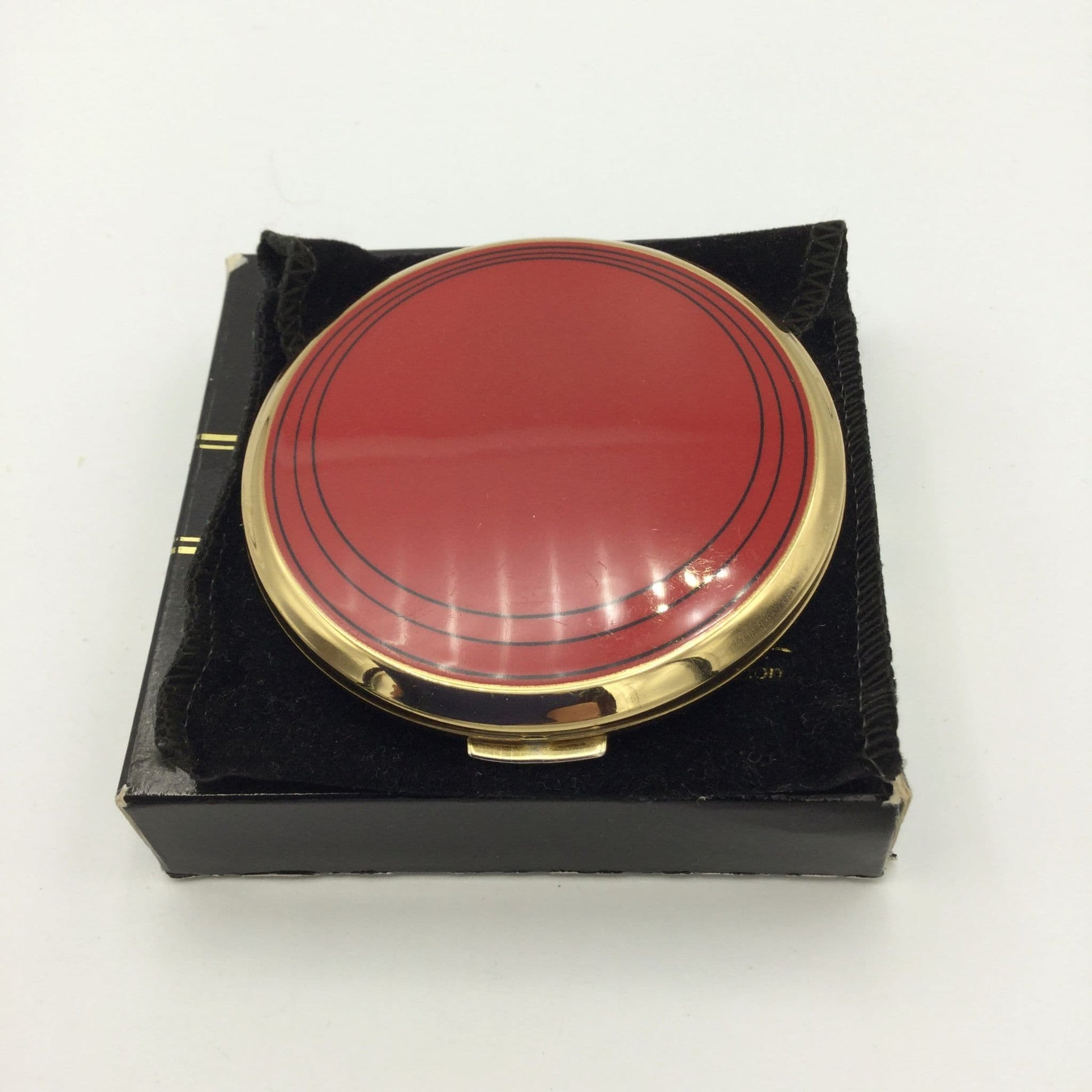 Bright red enamel on a Stratton mirror compact sitting on a  pouch and box